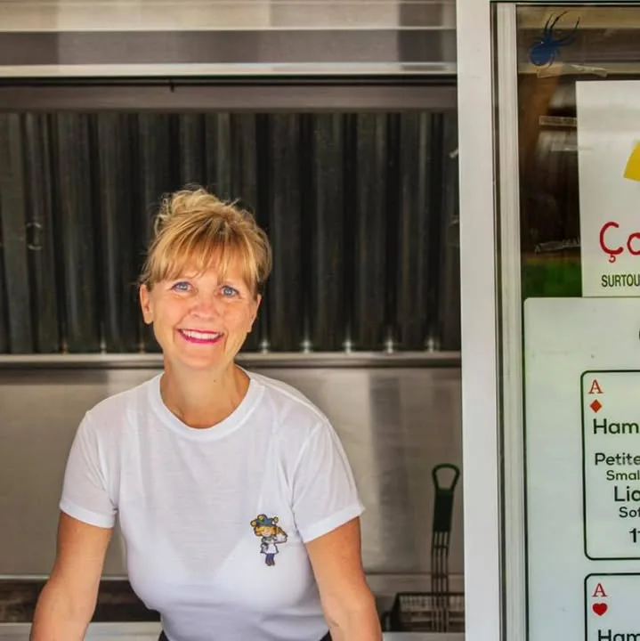La propriétaire devant le comptoir de service, avec le tableau du menu en arrière-plan
